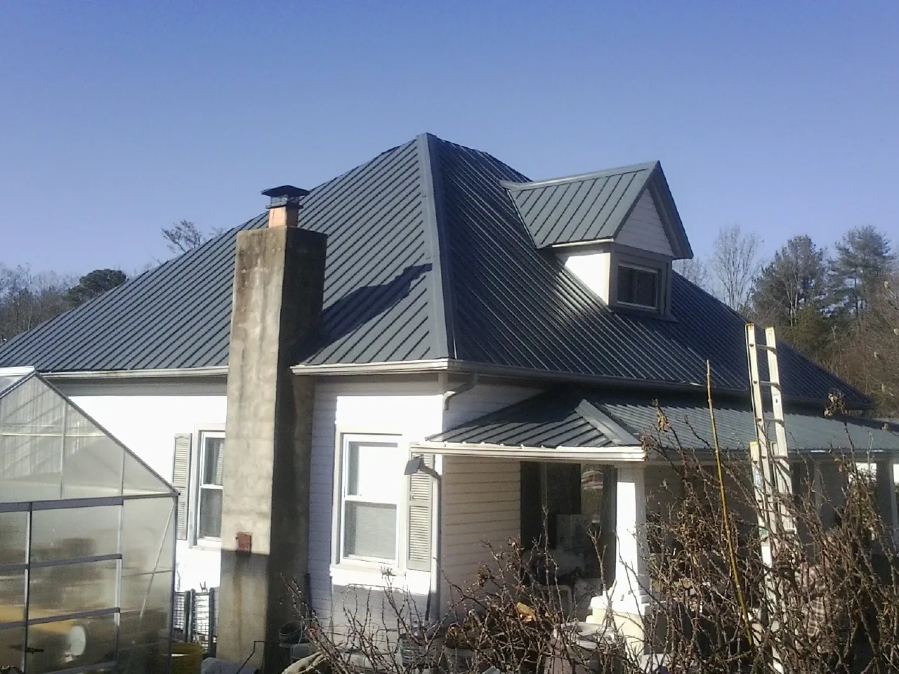 Dark blue standing seam metal roof on a white farmhouse with dormer — Slate & Tile Roof Repair by Roofing Brothers in Whitefield
