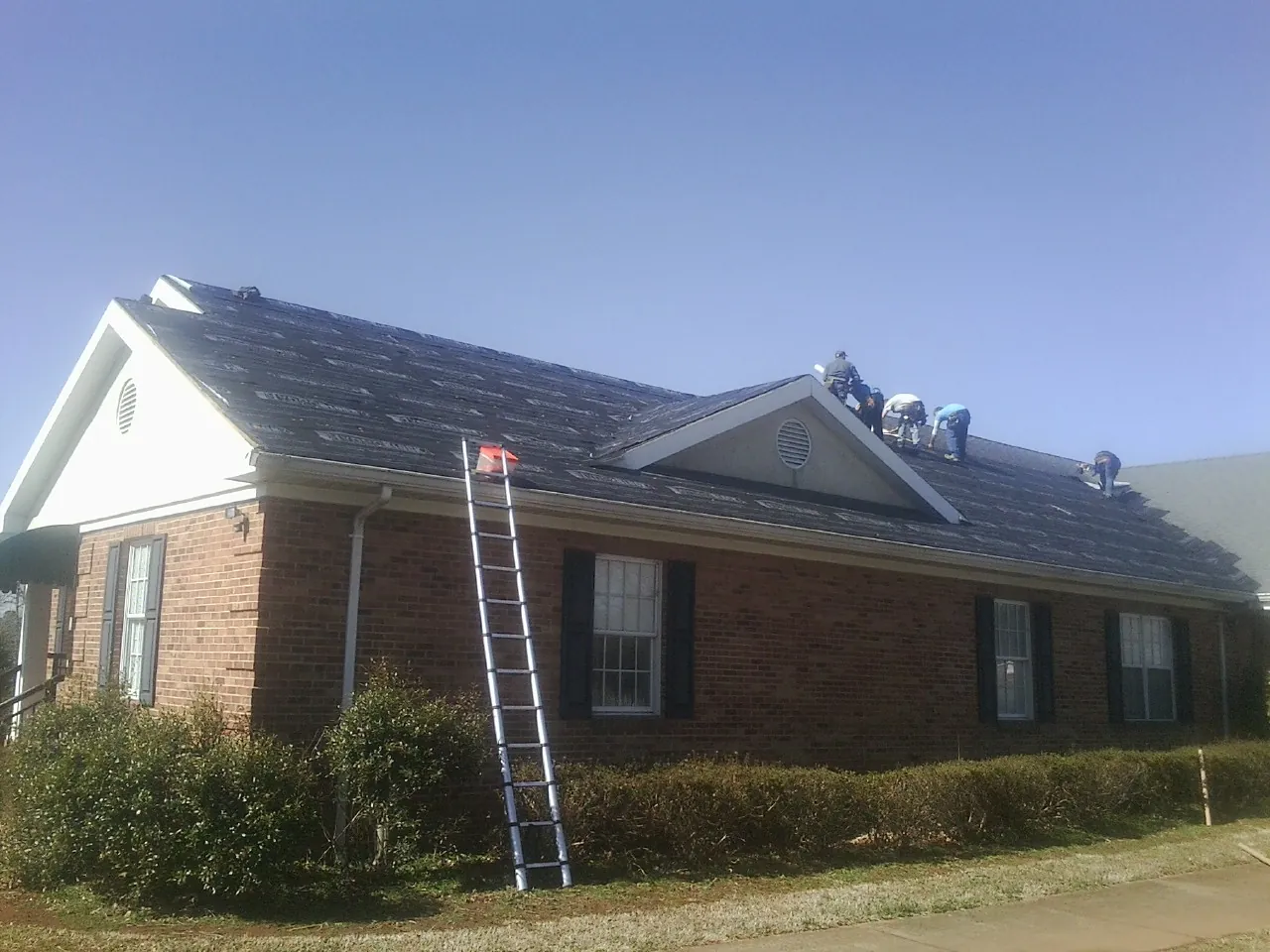 Crew tearing shingles off a brick ranch roof with a ladder set — Emergency Roof Repair work by our crew in Whitefield