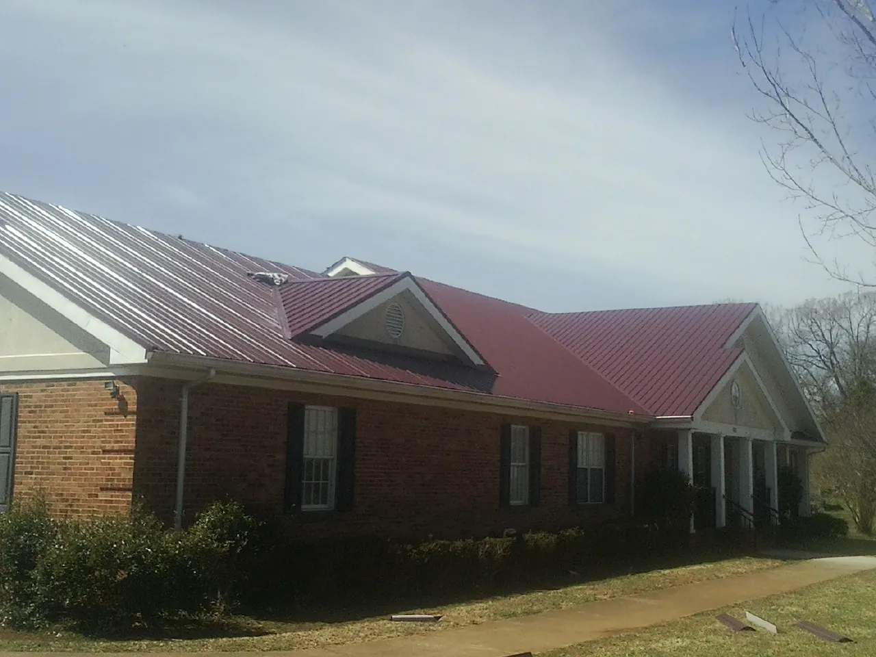Red metal roof with gabled entries on a long brick building, from a Hail Damage Roof Repair job in Whitefield