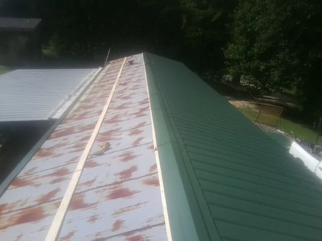 Old rusted panels beside newly installed green metal roofing — Wind Damage Roof Repair by Roofing Brothers in Whitefield