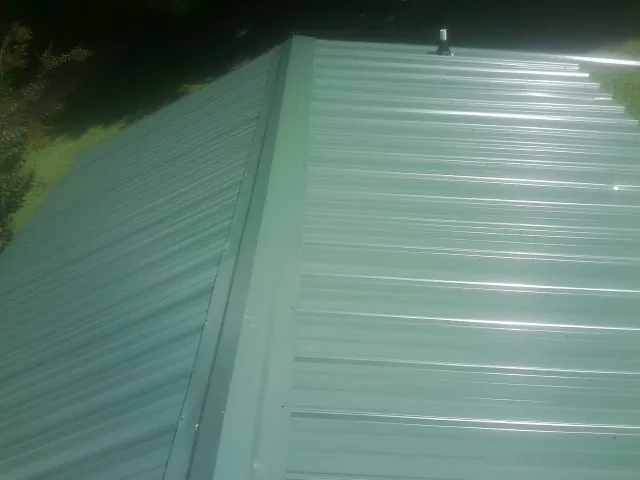 New green metal panels meeting at the ridge of a roof — Flat Roof Repair work by our crew in Whitefield