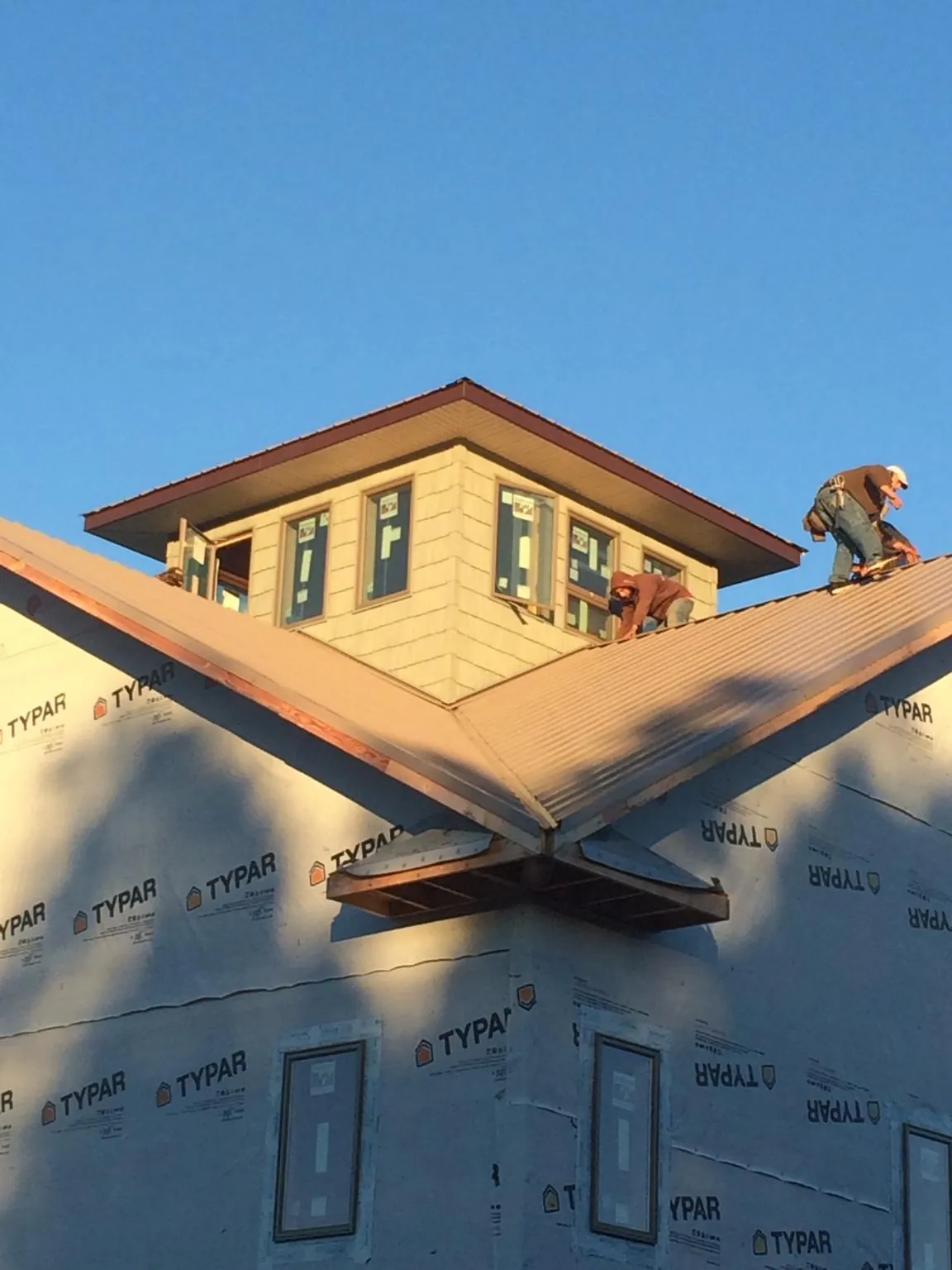 Roofers working around a rooftop cupola on a new metal roof at sunset — Roof Waterproofing in Whitefield by Roofing Brothers